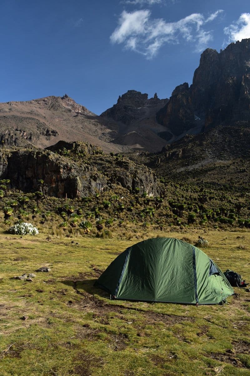 Green dome tent pitched at high altitude camp in the alpine hills with dramatic clouds